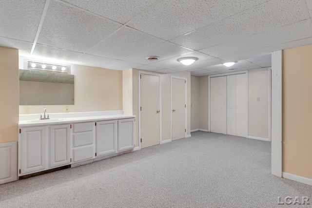 basement featuring a drop ceiling, light colored carpet, and wet bar