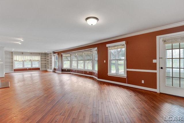 unfurnished living room with hardwood / wood-style flooring, crown molding, a wealth of natural light, and built in shelves