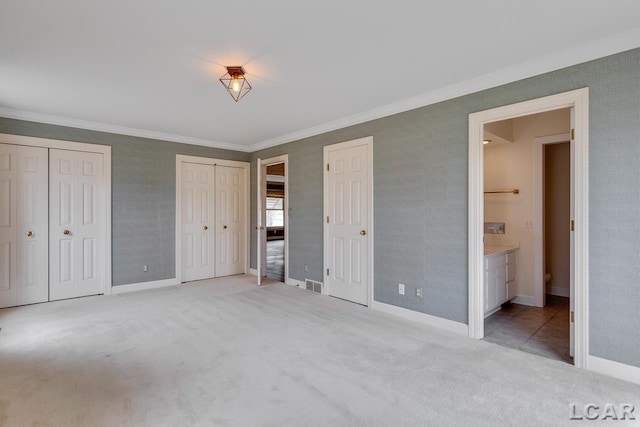 unfurnished bedroom featuring crown molding, two closets, light carpet, and connected bathroom