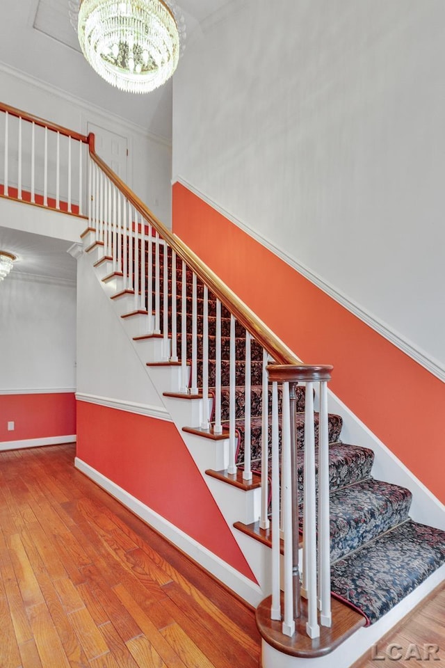 staircase with wood-type flooring, a notable chandelier, and crown molding