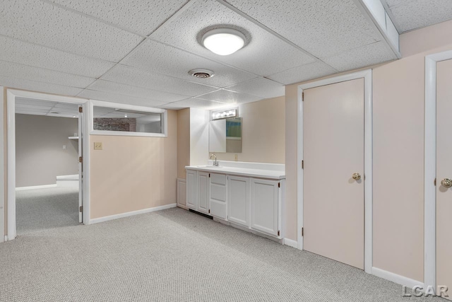 basement featuring sink, a paneled ceiling, and light colored carpet