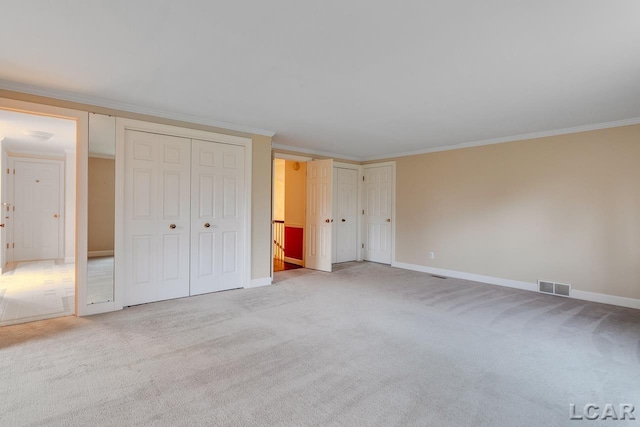 unfurnished bedroom featuring multiple closets, ornamental molding, and light carpet