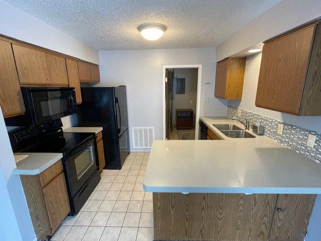 kitchen with tasteful backsplash, black appliances, light tile patterned floors, kitchen peninsula, and a textured ceiling