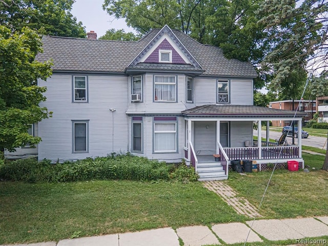 victorian home with cooling unit, a front yard, and covered porch