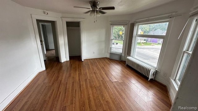 unfurnished bedroom featuring ceiling fan, radiator heating unit, a textured ceiling, dark hardwood / wood-style flooring, and a closet