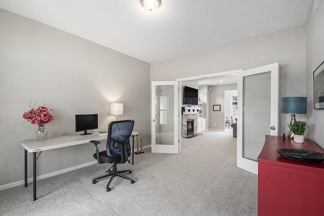 carpeted office space featuring a stone fireplace and french doors