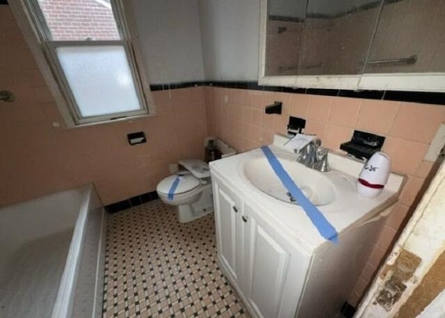 bathroom with vanity, a washtub, tile walls, and toilet