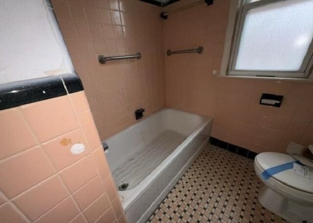 bathroom featuring toilet, a bath, and tile walls