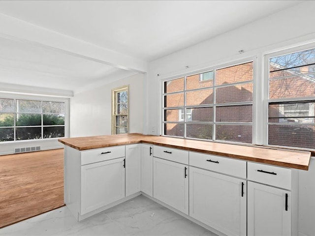 kitchen with butcher block countertops, beamed ceiling, and white cabinets