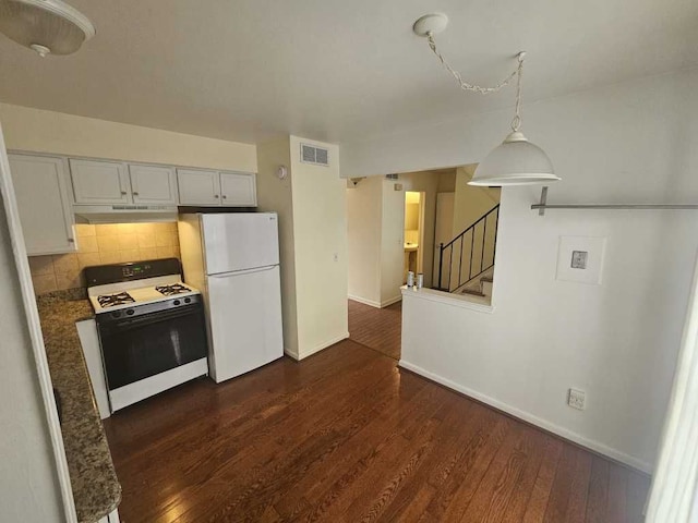 kitchen featuring dark wood-type flooring, hanging light fixtures, white refrigerator, gas range oven, and decorative backsplash