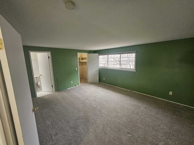 unfurnished bedroom featuring ensuite bath, a spacious closet, a closet, and carpet