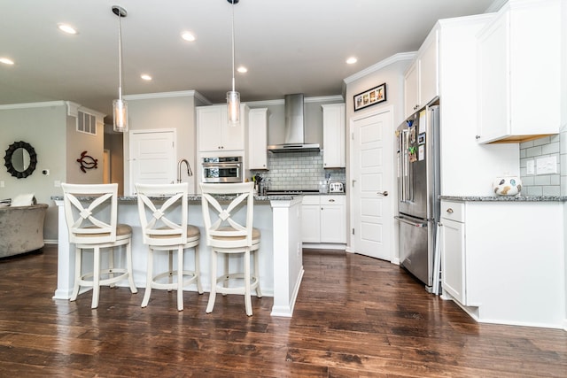 kitchen featuring appliances with stainless steel finishes, white cabinetry, dark stone counters, hanging light fixtures, and wall chimney exhaust hood