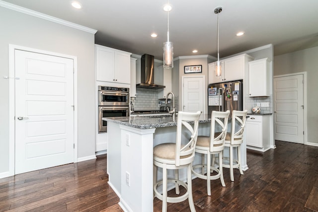 kitchen with sink, a center island with sink, wall chimney range hood, stainless steel appliances, and white cabinets