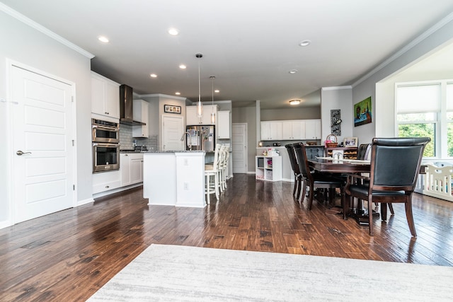 kitchen with wall chimney range hood, pendant lighting, a center island with sink, and white cabinets