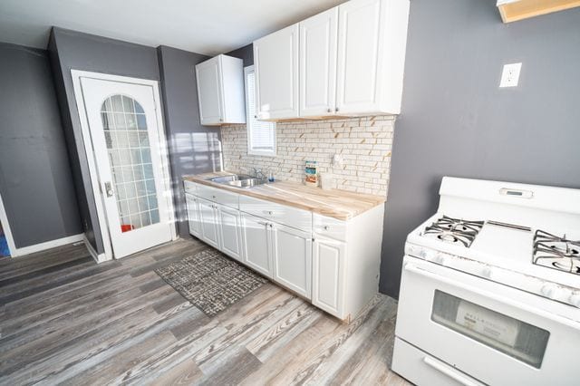 kitchen featuring white cabinetry, wood-type flooring, white gas range, and sink