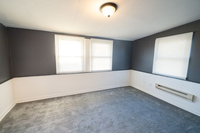 spare room with dark carpet and a baseboard heating unit