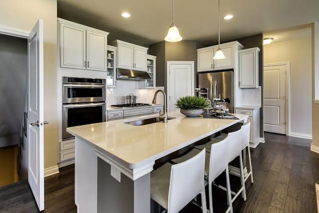 kitchen with sink, hanging light fixtures, stainless steel appliances, a kitchen island with sink, and white cabinets