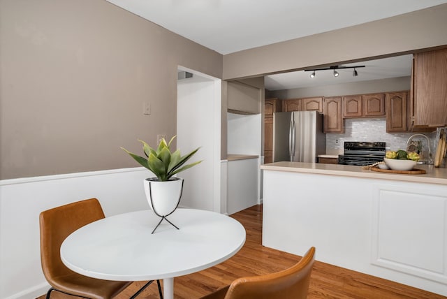 kitchen with stainless steel refrigerator, sink, decorative backsplash, black electric range, and light wood-type flooring