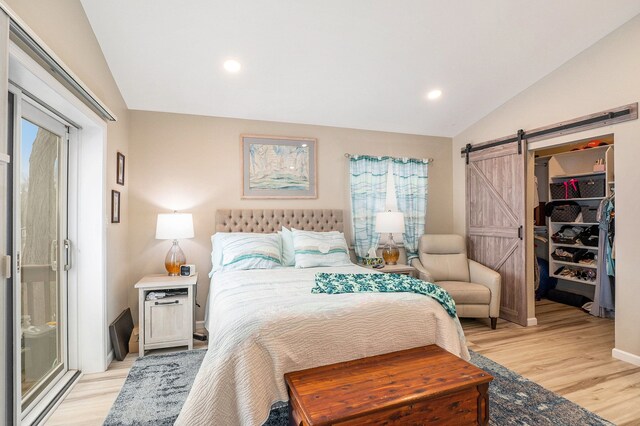 bedroom with vaulted ceiling, a barn door, and light wood-type flooring