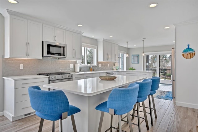 kitchen with appliances with stainless steel finishes, a peninsula, white cabinets, and light countertops