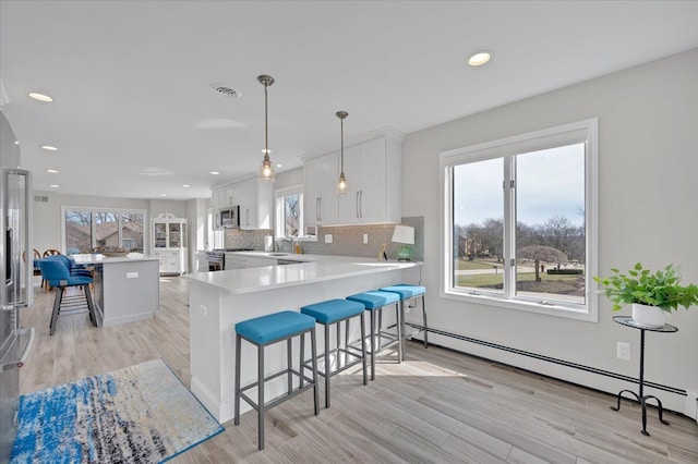 kitchen featuring visible vents, a breakfast bar, stainless steel appliances, a baseboard heating unit, and tasteful backsplash