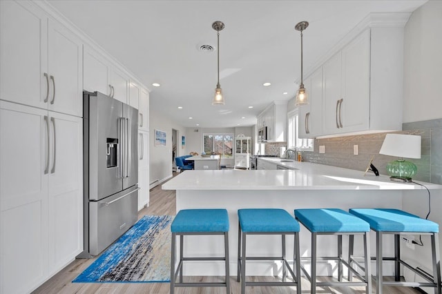 kitchen with backsplash, appliances with stainless steel finishes, a peninsula, white cabinets, and light countertops