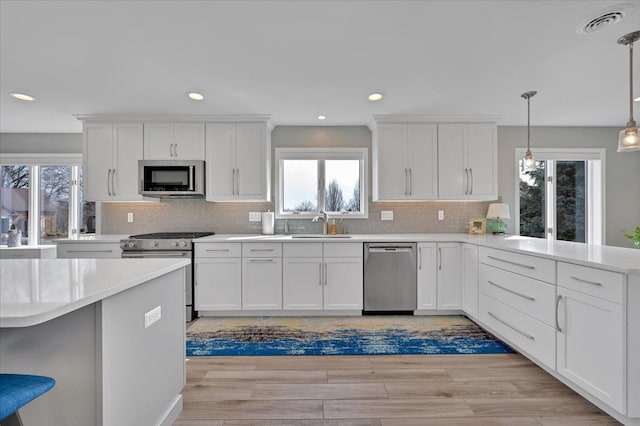 kitchen featuring a peninsula, stainless steel appliances, light countertops, white cabinets, and light wood-type flooring