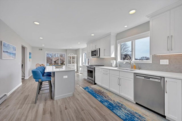 kitchen with a breakfast bar, light wood-type flooring, white cabinets, stainless steel appliances, and a sink