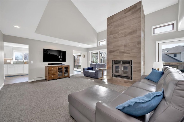 living area featuring high vaulted ceiling, a fireplace, a baseboard radiator, baseboards, and light colored carpet