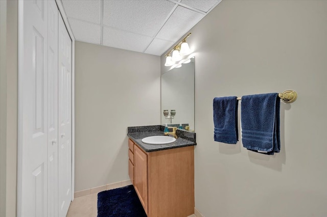 bathroom with tile patterned flooring, baseboards, a drop ceiling, a closet, and vanity