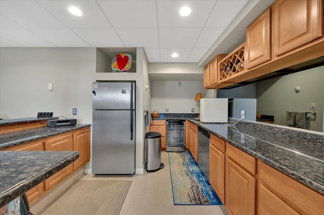 kitchen with dark stone countertops, light tile patterned floors, brown cabinetry, a drop ceiling, and stainless steel appliances