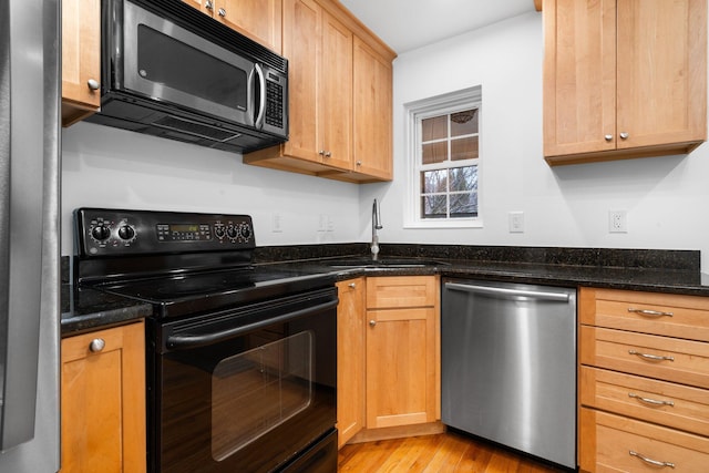 kitchen with appliances with stainless steel finishes, light hardwood / wood-style floors, sink, and dark stone counters