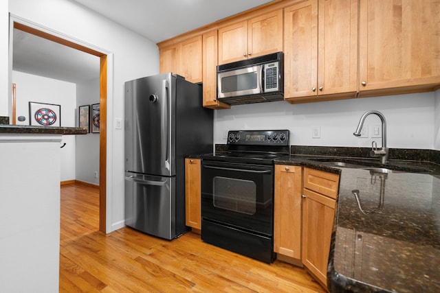 kitchen featuring dark stone countertops, sink, light wood-type flooring, and appliances with stainless steel finishes