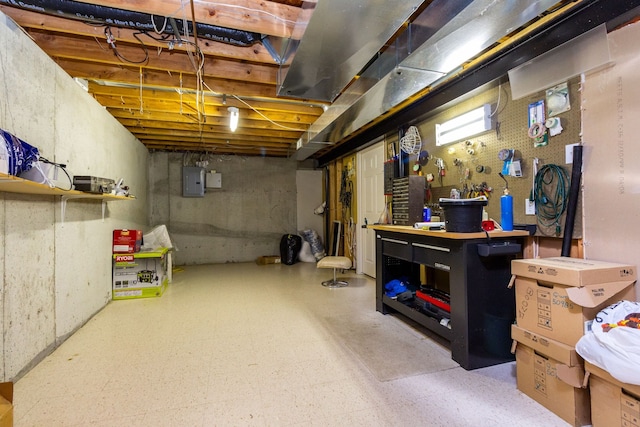 basement featuring tile patterned floors, a workshop area, and electric panel