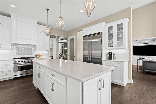 kitchen with white cabinetry, decorative light fixtures, premium appliances, dark hardwood / wood-style floors, and a kitchen island