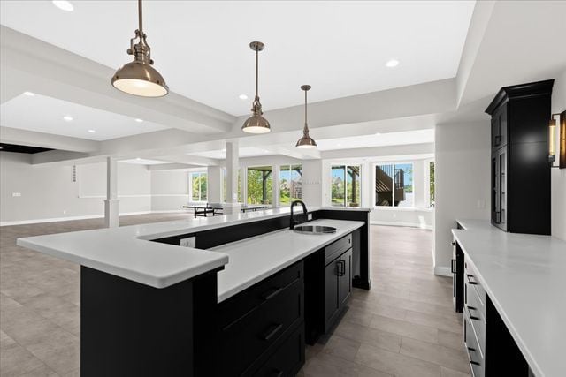 kitchen featuring a kitchen island with sink, hanging light fixtures, sink, and beamed ceiling