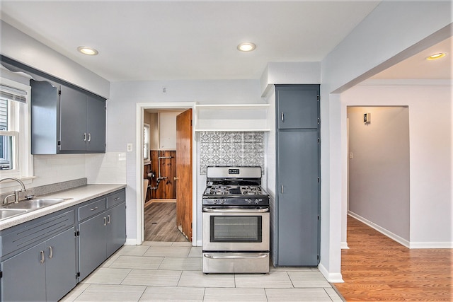 kitchen with stainless steel range with gas stovetop, light hardwood / wood-style floors, sink, and backsplash