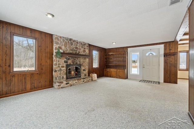 unfurnished living room with a stone fireplace, wooden walls, a textured ceiling, and carpet flooring