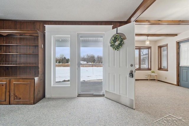 doorway to outside with light colored carpet, beam ceiling, and a textured ceiling