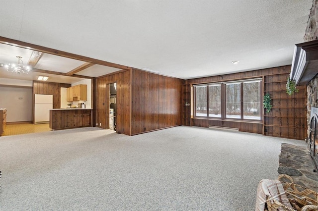 unfurnished living room with a stone fireplace, wood walls, light carpet, baseboard heating, and a notable chandelier