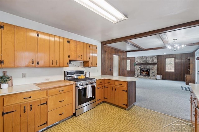 kitchen with beam ceiling, gas range, wooden walls, and kitchen peninsula