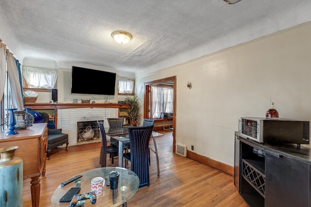 dining room with wood-type flooring, a fireplace, a textured ceiling, and a wealth of natural light