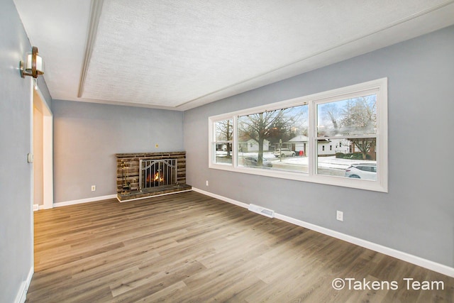 unfurnished living room with hardwood / wood-style flooring, a stone fireplace, and a textured ceiling