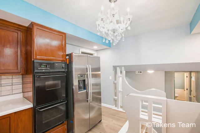 kitchen featuring double oven, light wood-type flooring, backsplash, stainless steel fridge, and an inviting chandelier