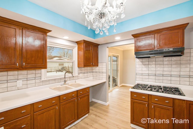 kitchen with sink, hanging light fixtures, stainless steel gas stovetop, light hardwood / wood-style floors, and decorative backsplash