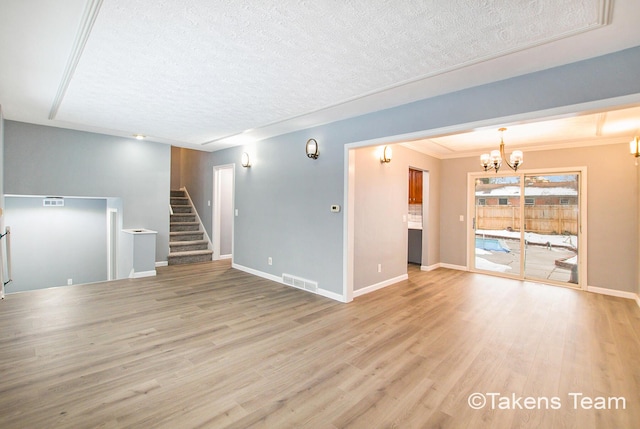 unfurnished living room featuring ornamental molding, light hardwood / wood-style floors, a textured ceiling, and a notable chandelier