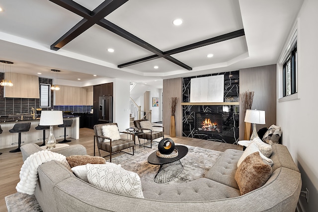 living room featuring coffered ceiling, beam ceiling, a high end fireplace, and light hardwood / wood-style floors