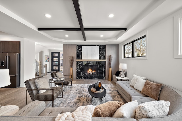 living room with coffered ceiling, a high end fireplace, light hardwood / wood-style flooring, and beamed ceiling