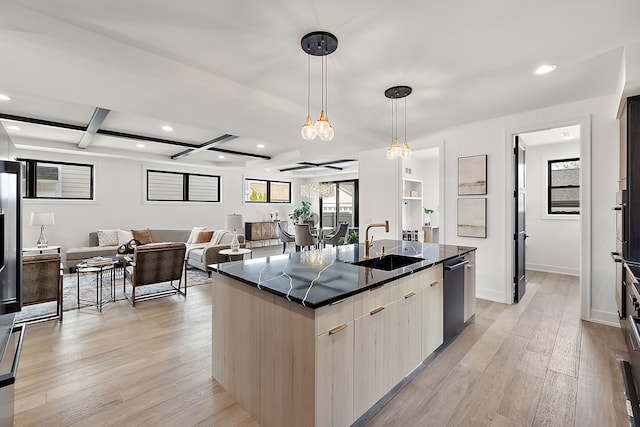 kitchen with hanging light fixtures, sink, an island with sink, and light wood-type flooring