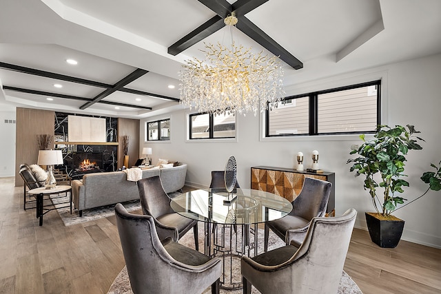 dining space with a fireplace, a chandelier, coffered ceiling, light hardwood / wood-style floors, and beam ceiling